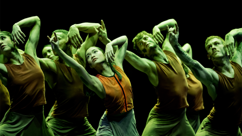 Dancers wearing orange lit by green stage lights.