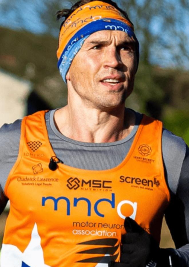 A photo of athlete Kevin Sinfield running, wearing an orange vest and hat. 