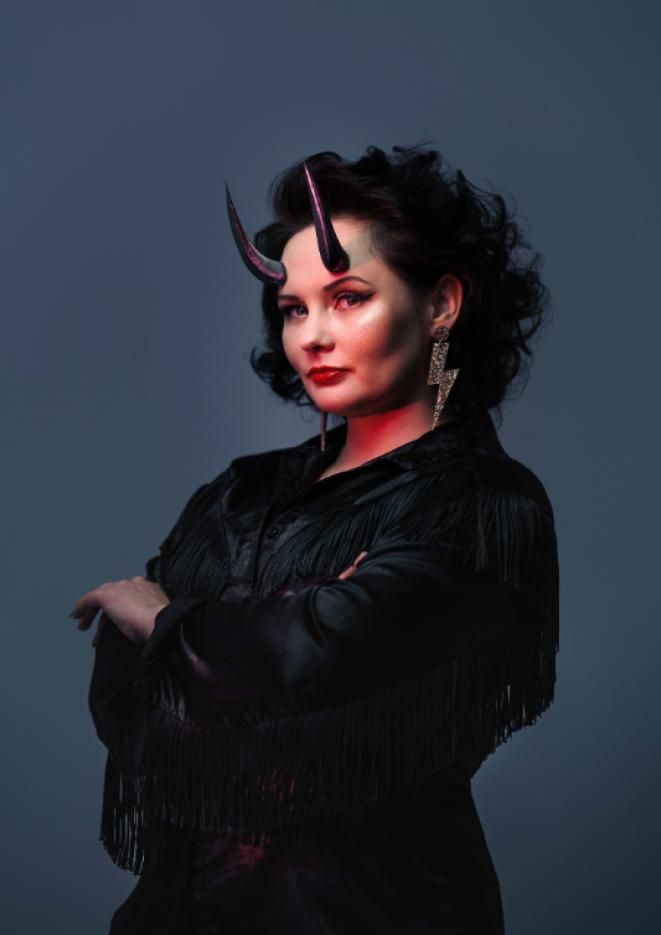 Female comedian Rachel Fairburn wears an all black outfit with costume horns.