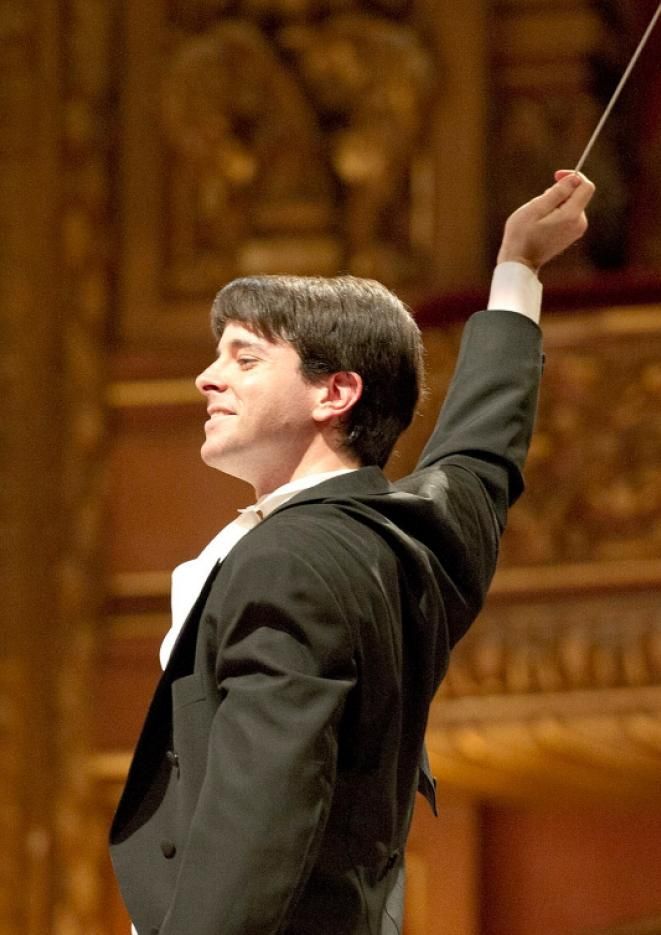 Conductor Mariano Chiacchiarini of the Buenos Aires Symphony Orchestra wears smart attire with his conductors baton in the air.