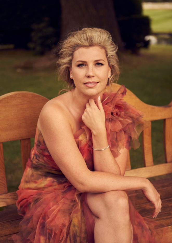 Singer Alexandra Lowe sits on a bench wearing a floral dress.