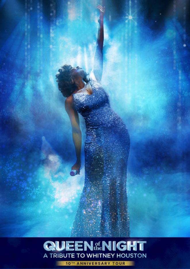 Tribute artist of Whitney Houston stands against a blue background wearing a long blue sparkly dress.