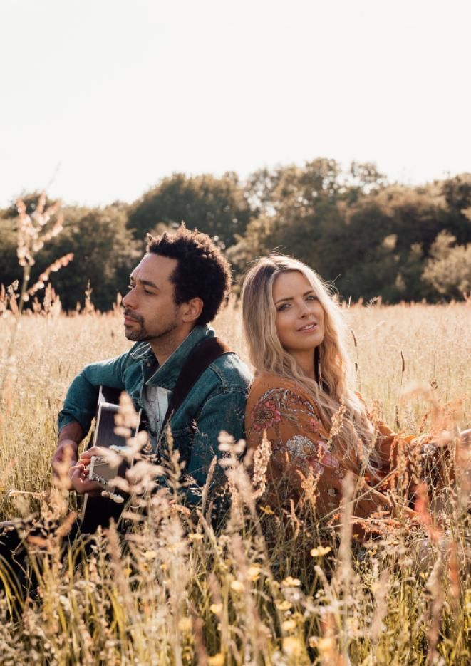 A musical duo sit in a wheat field on a sunny day.