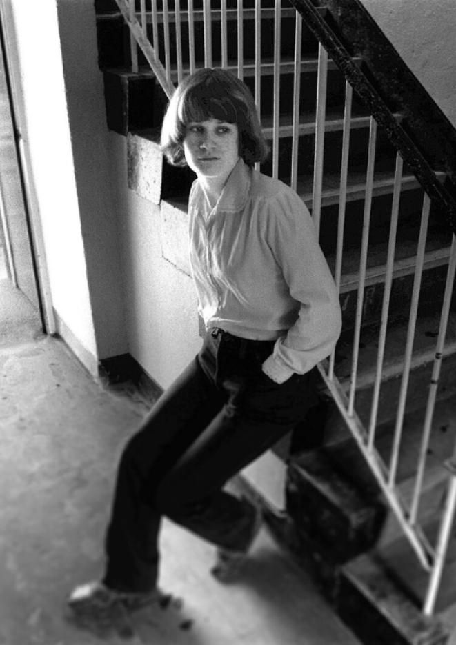 A black and white photograph of Andrea Dunbar leaning against a staircase railing.