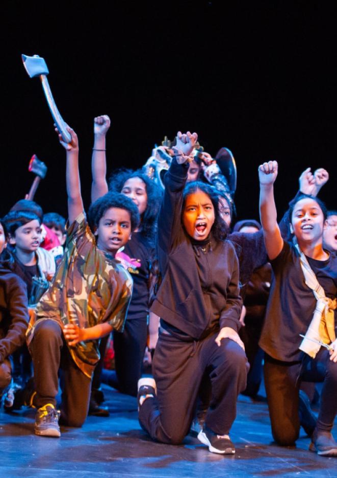 A group of young children performing on stage in front of a black background.